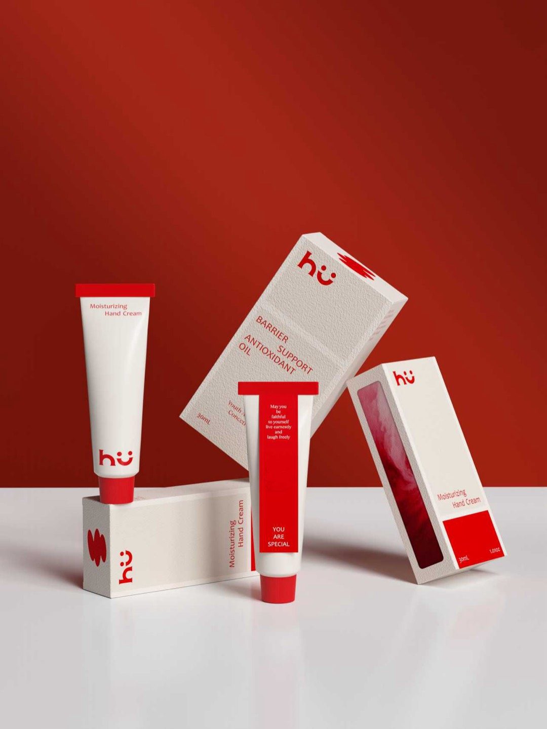 The hü hand cream tube with its window carton and barrier oil box against a red ground