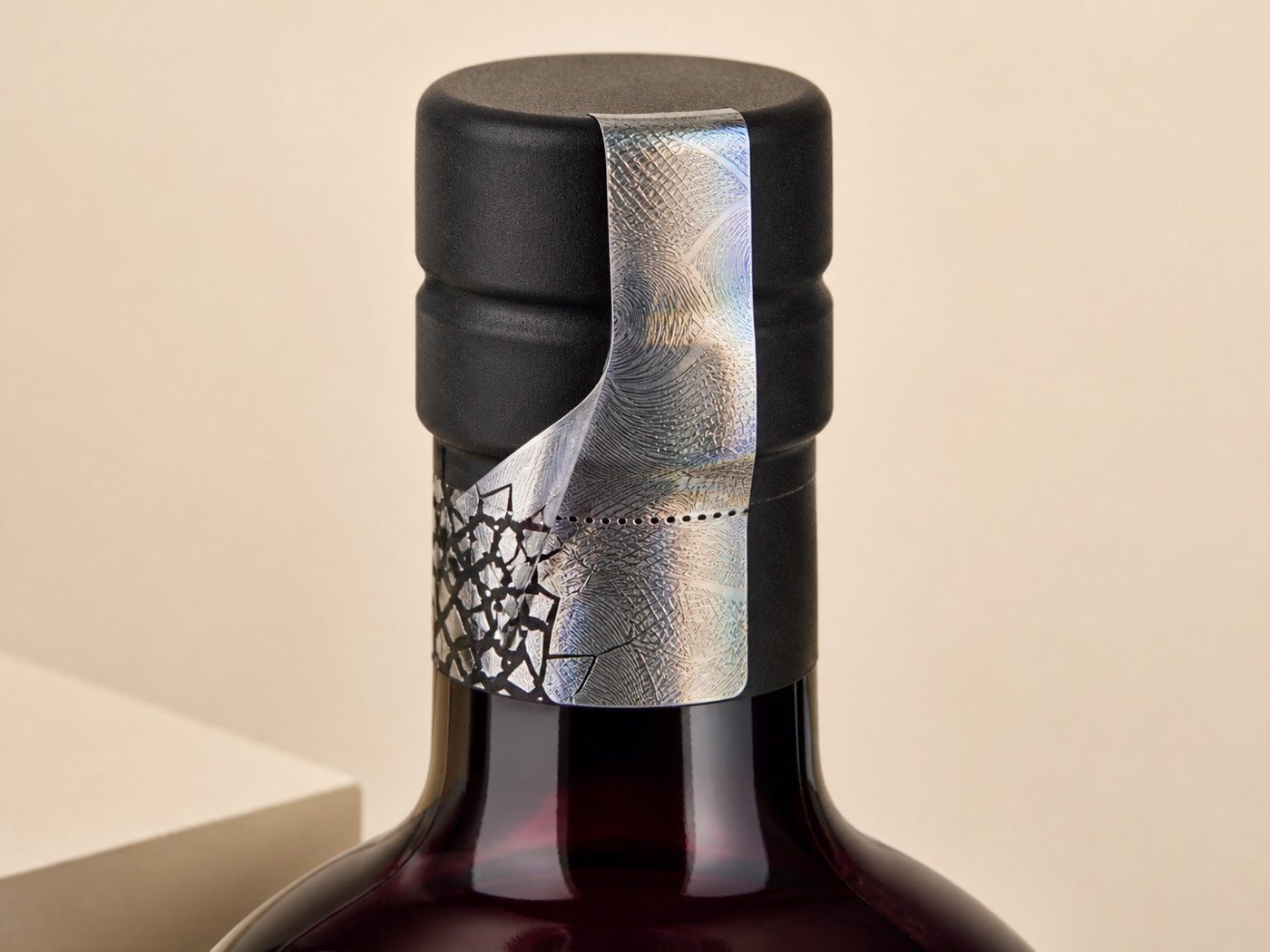 Destructible holographic neck seal crossing the closure seam of a blank claret glass bottle
