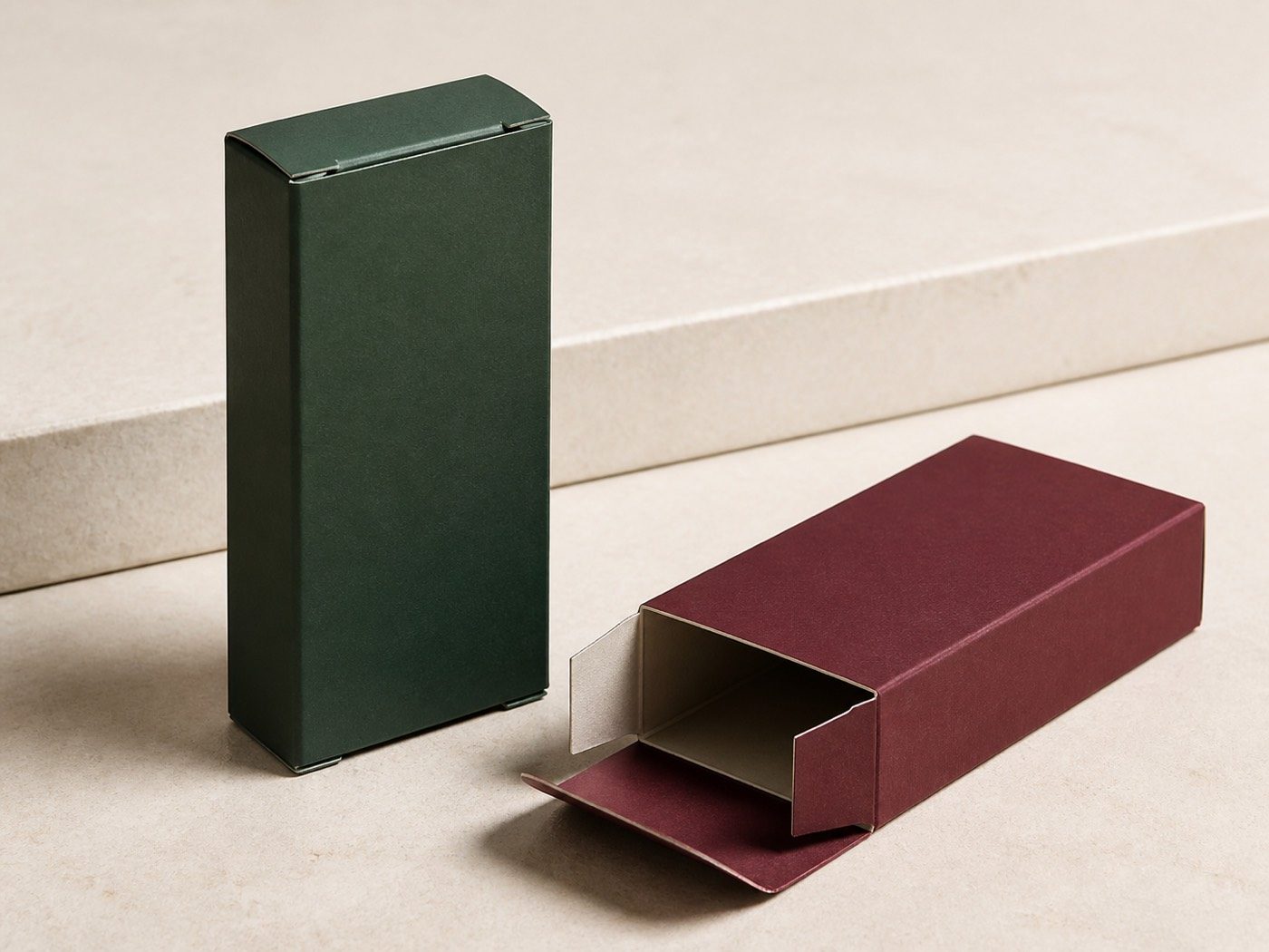 Closed forest-green folding carton beside a claret tuck-end carton with its end flaps open