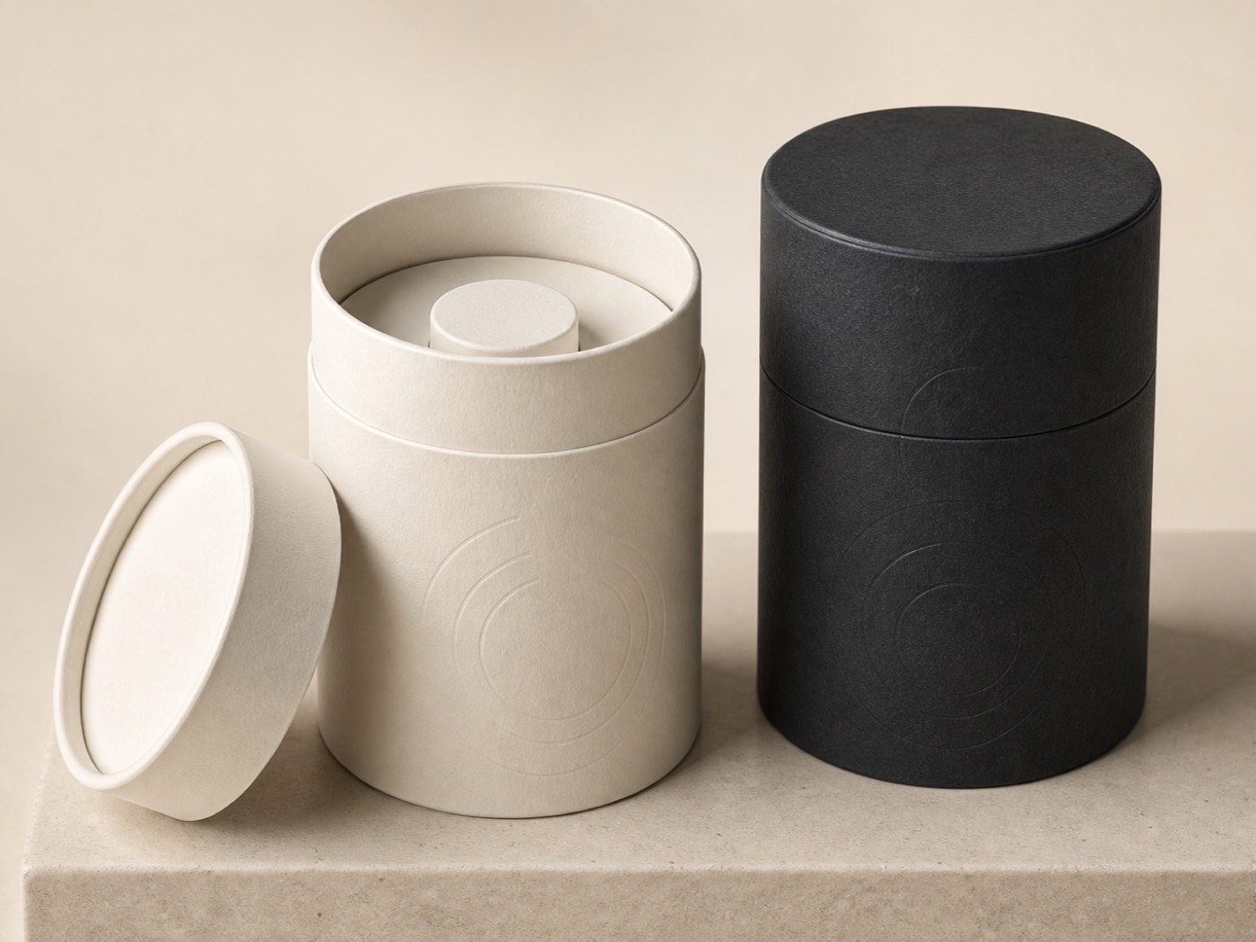 Ivory paper tube open to show its fitted insert beside a closed charcoal cylinder